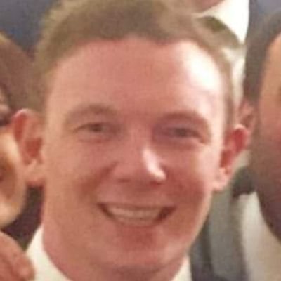 A smiling person in a suit at a social gathering.