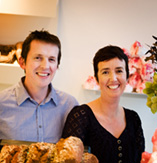 Two people smiling behind a display of bread and pastries.