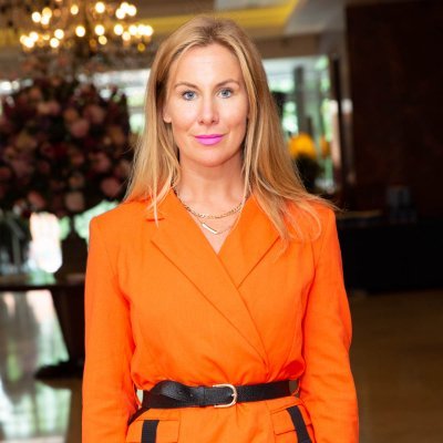 Person in an orange outfit standing indoors with a blurred background.