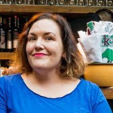 Person in a blue shirt smiling in a kitchen setting.
