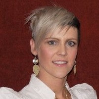 Person with short blonde hair and earrings against a red background.